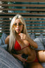 Woman in a red bikini sitting on a couch outdoors, holding a drink.