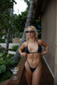 Woman in a black bikini standing outdoors with palm trees and a cocktail in the background